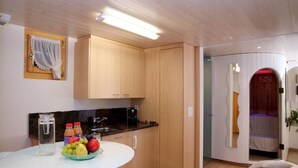 Cocina compacta con armarios de madera, encimera blanca y una mesa redonda con fruta y una botella de agua.