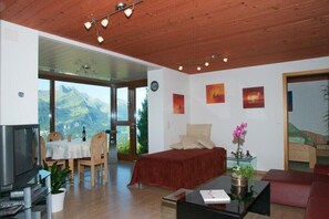 Relax in a stylish living room with a sofa, dining table, and TV, offering a view of the surrounding mountains.