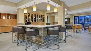 Een moderne keuken met een centraal eiland, barkrukken en een zithoek met tafels en stoelen.
