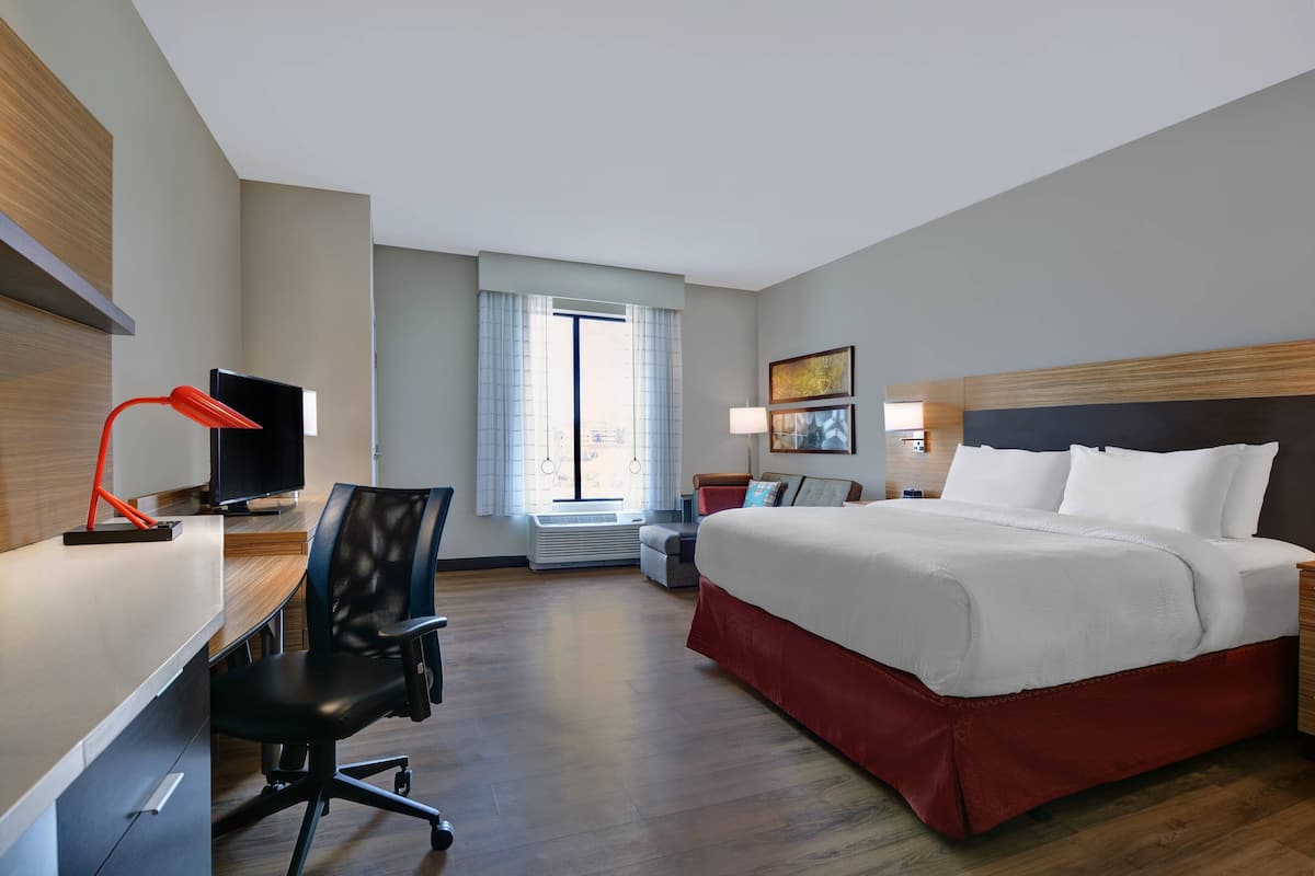 Une chambre d’hôtel équipée d’un lit, d’un bureau, d’une chaise, d’une télévision et d’une fenêtre avec des rideaux.