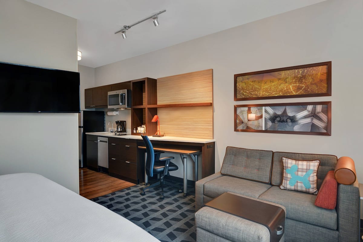 Une chambre d’hôtel compacte équipée d’une kitchenette, d’un canapé, d’un bureau et d’un téléviseur à écran plat.