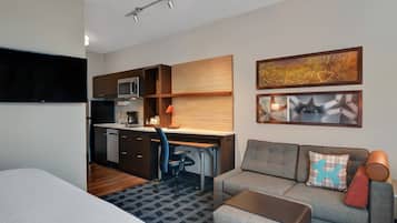 Una habitación de hotel compacta con kitchenette, un sofá, un escritorio y un televisor de pantalla plana.