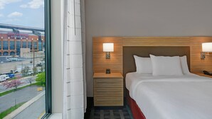 Een hotelkamer met een groot raam, een bed met witte lakens, een houten hoofdeinde en een nachtkastje met een lamp.