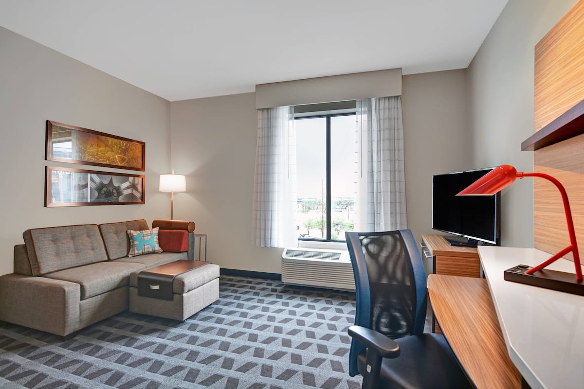 Une chambre d’hôtel équipée d’un canapé, d’un bureau, d’une chaise, d’une télévision et d’une fenêtre avec des rideaux.