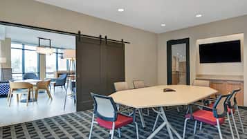A conference room with a large table, six chairs, and a TV on the wall.