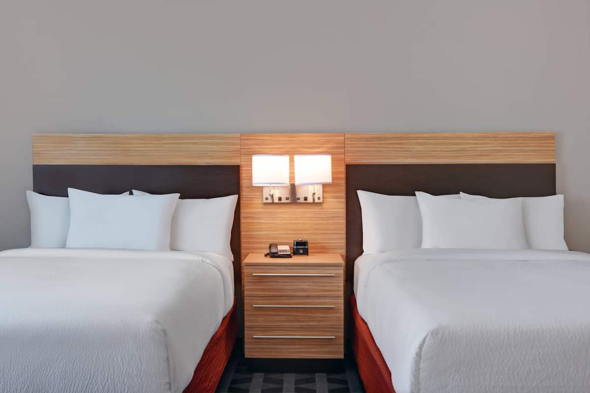 Une chambre d’hôtel avec deux lits, une tête de lit en bois, des lampes de chevet, une petite table et une commode.