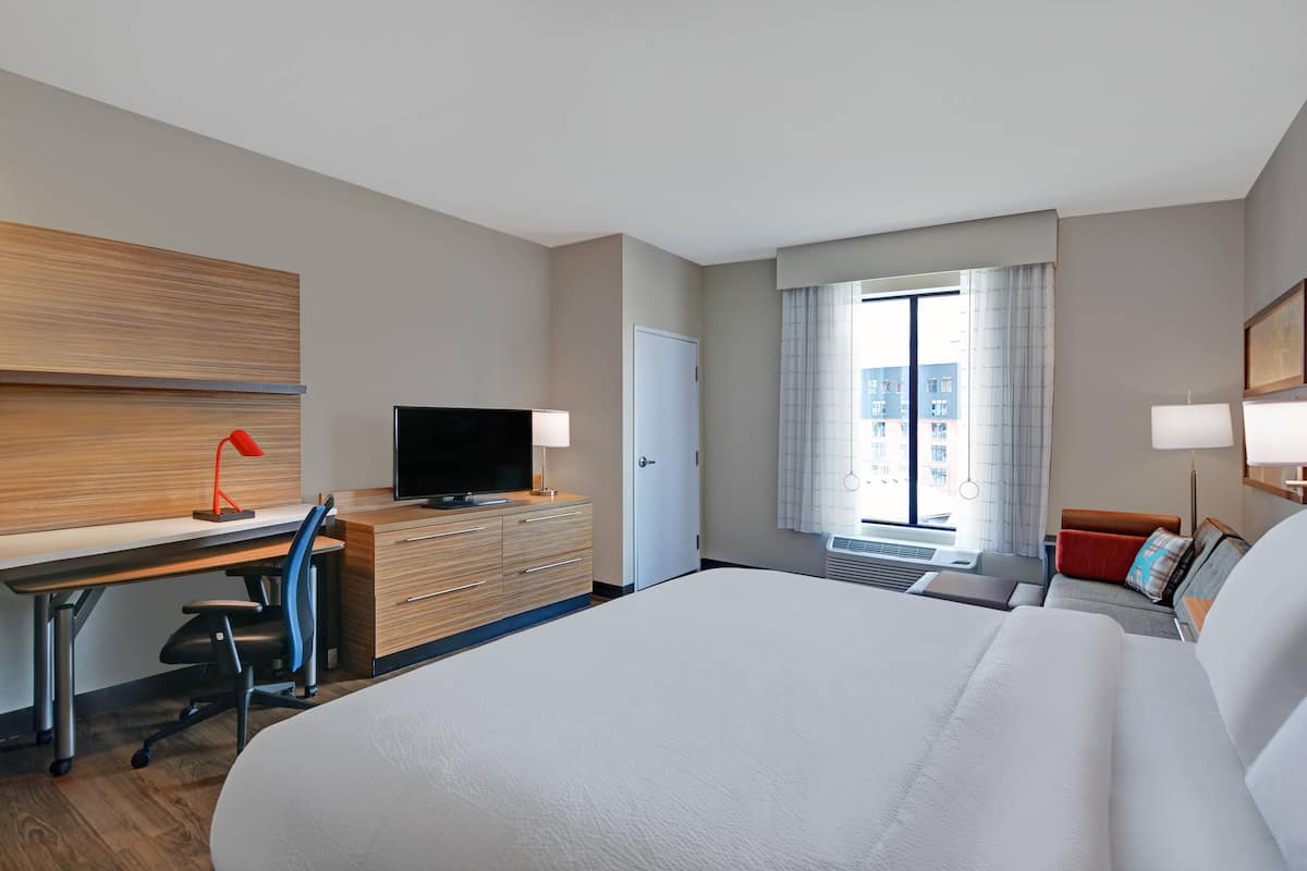 Une chambre d’hôtel avec un grand lit, un bureau avec un ordinateur, une télévision et une fenêtre avec des rideaux.