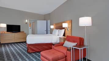A hotel room with a bed, a TV, a desk with a chair, and a floor lamp.