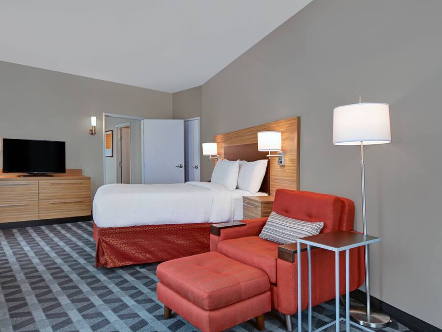 A hotel room with a bed, a TV, a desk with a chair, and a floor lamp.