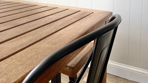 Ett träbord med en metallstol framför, en vit vägg med en skylt som lyder ”välkommen till vårt hus vid stranden” och en vit dörr.