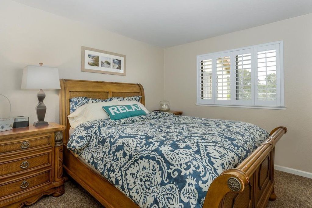 A bedroom with a wooden bed, a nightstand, a lamp, a framed picture on the wall, and a window with blinds.