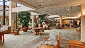 Un hall d’entrée spacieux avec un espace salon central, de grandes plantes en pot et un escalier menant aux étages supérieurs.