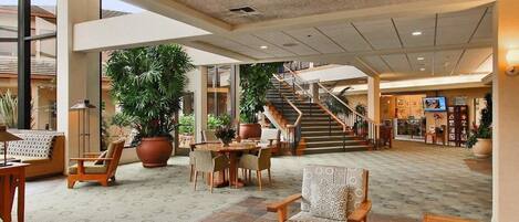 A spacious lobby with a central seating area, large potted plants, and a staircase leading to upper floors.