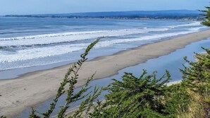 Une plage avec des vagues, une rive sablonneuse et des collines à l’horizon.