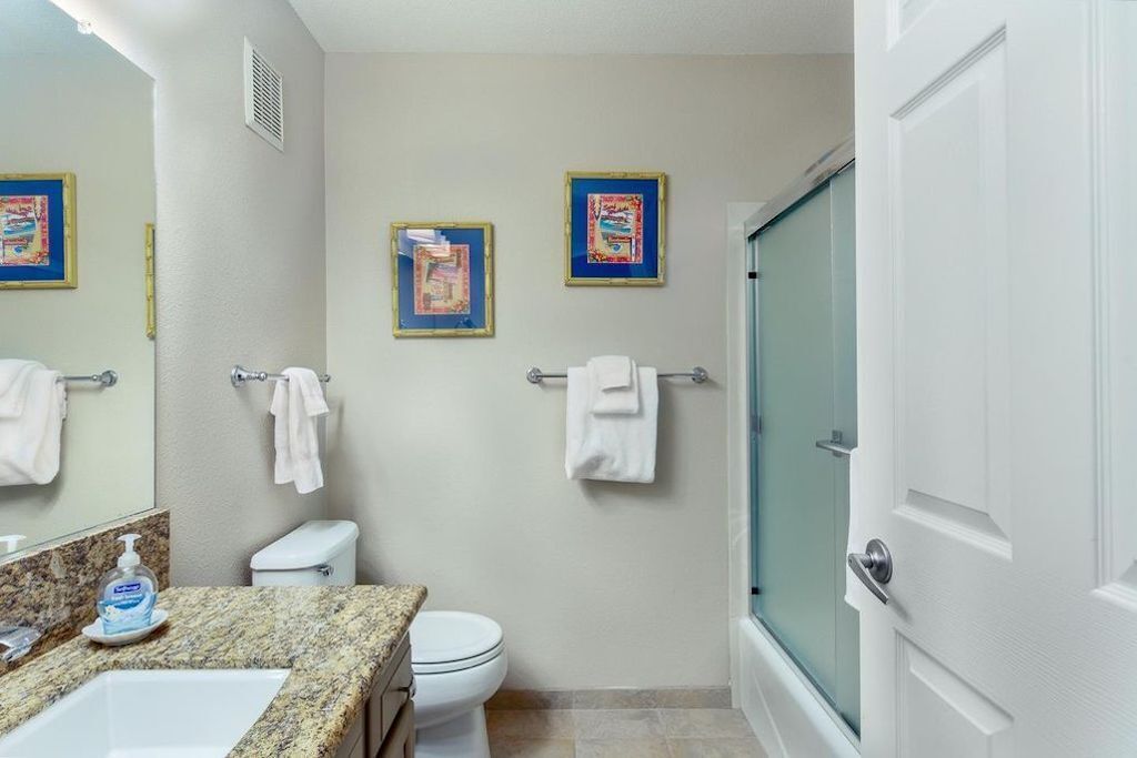 A bathroom with a sink, toilet, and shower. There are towels hanging on the wall and a framed picture.