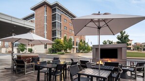 An outdoor patio area with tables and chairs, a large umbrella, and a TV screen. - AC Hotel Pittsburgh Southpointe (Canonsburg)
