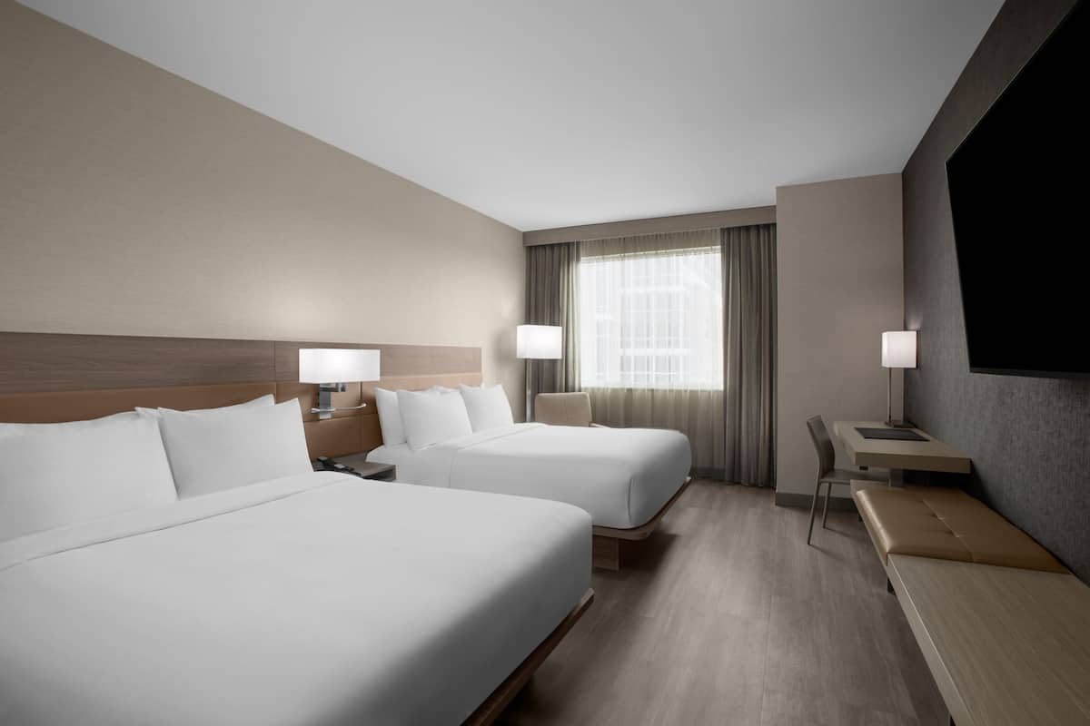 A hotel room with two beds, a desk, and a TV.