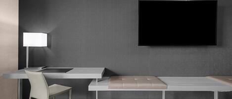 Una habitación moderna con escritorio, silla, banco y televisor de pantalla plana montado en la pared.