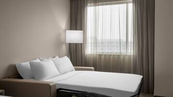 Habitación de hotel con cama, mesita de noche, lámpara y ventana con cortinas.