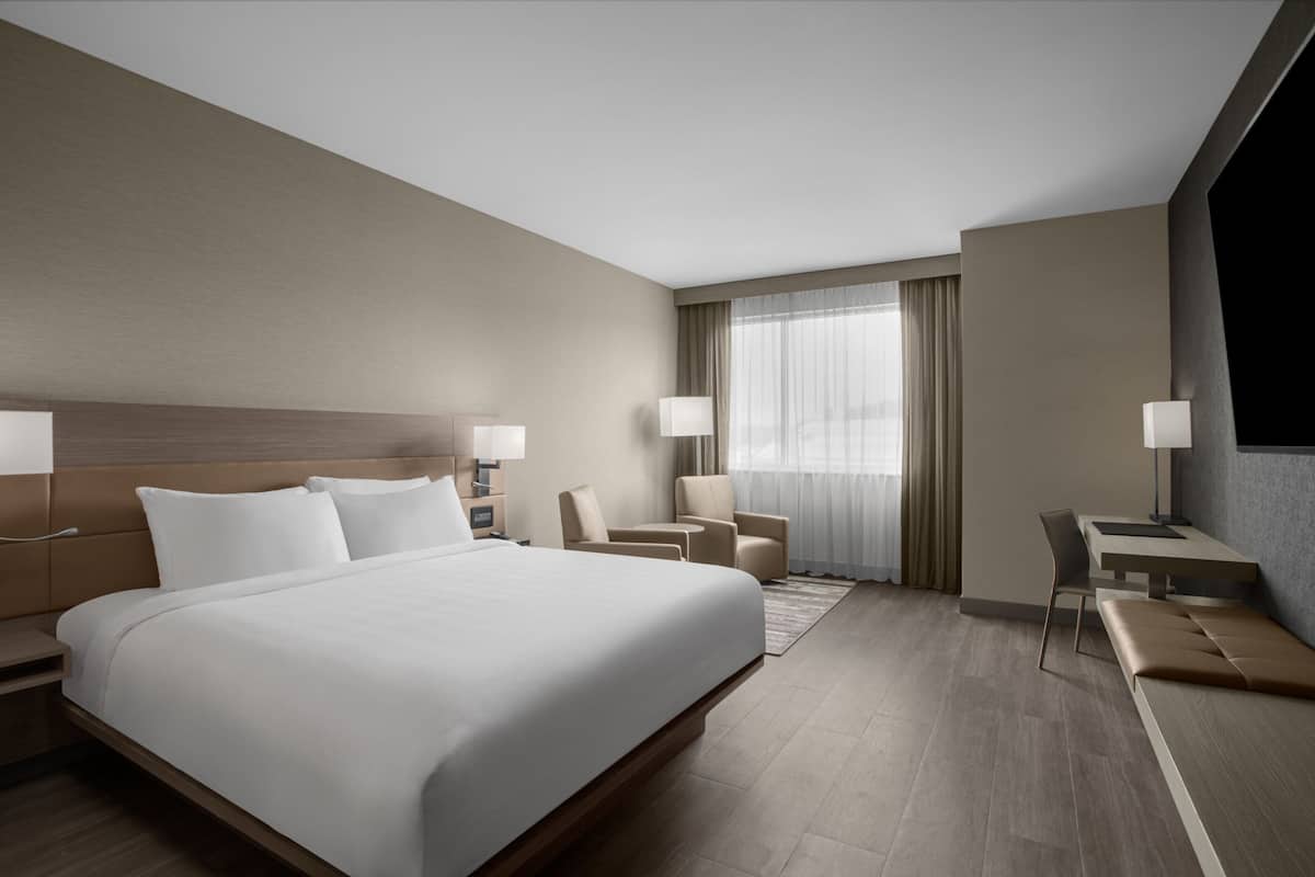 A hotel room with a large bed, two bedside tables, a desk, a chair, and a sofa.