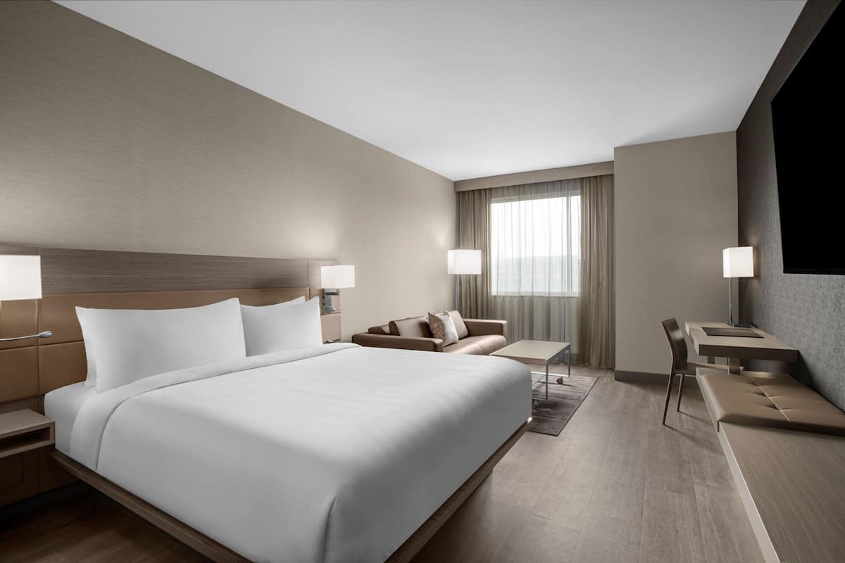 A modern hotel room with a large bed, a sofa, a desk, and two lamps.