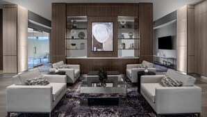 A modern living room with a glass coffee table, two white sofas, a TV, and a wall-mounted shelf with decorative items. - AC Hotel Pittsburgh Southpointe (Canonsburg)