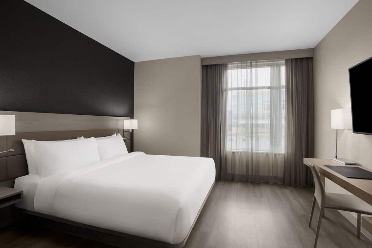 A modern hotel room with a large bed, a desk, and a television.