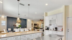 Una cocina moderna con armarios blancos, encimera de granito, iluminación colgante y ventilador de techo.