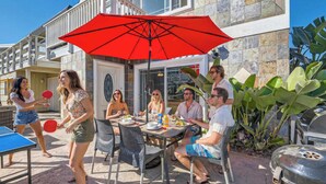 Un patio al aire libre con una mesa, sillas y un paraguas rojo.