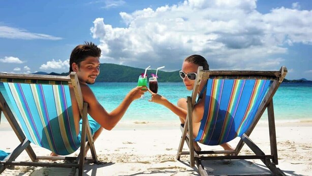 Dos personas brindando con bebidas en la playa.
