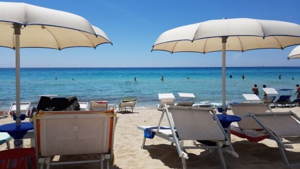 Een strand met witte parasols en ligbedden.