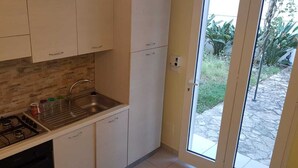 Een kleine keuken met een gasfornuis, een spoelbak en witte keukenkastjes.