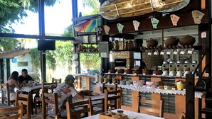 Un café rústico con mesas y sillas de madera, pared de ladrillo y una variedad de cerámica y utensilios de cocina exhibidos en estanterías.