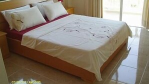 Un letto rifatto con lenzuola bianche, una testiera in legno e un cuscino decorativo rosso.