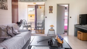 En moderne stue med sofa, sofabord og tv. En dør fører ud til en balkon med udsigt.