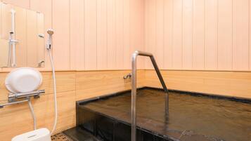 A sauna room with a black heated floor, a white heater, and a white toilet.