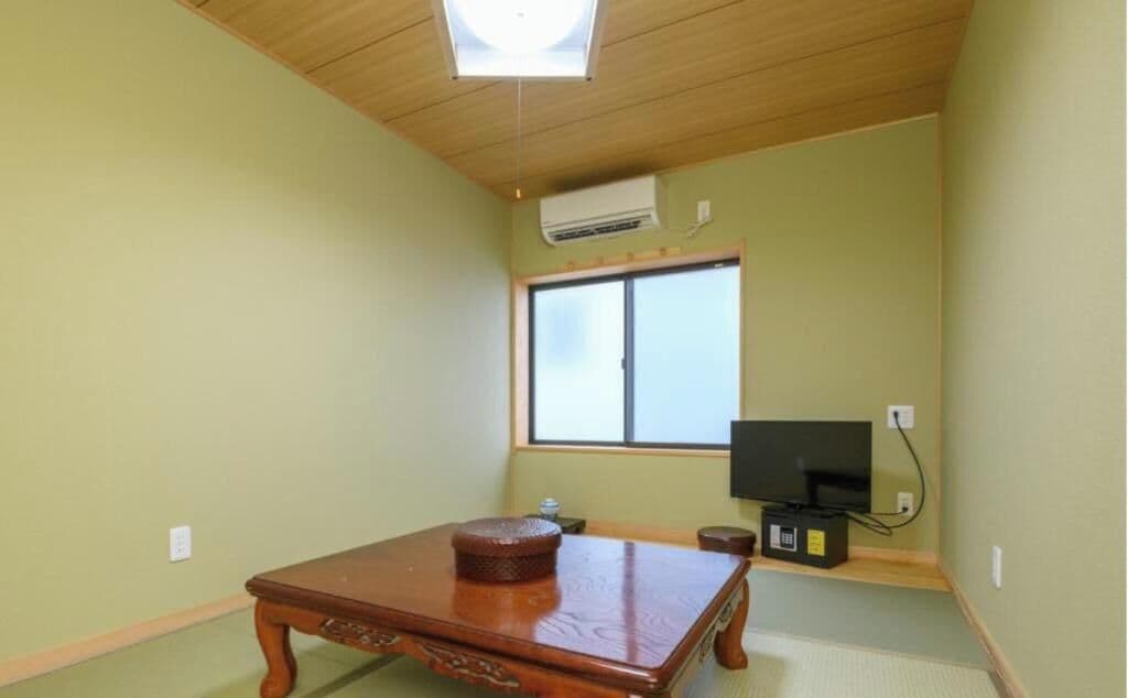 A traditional Japanese room with tatami flooring, a wooden table, a television, and a sliding door.