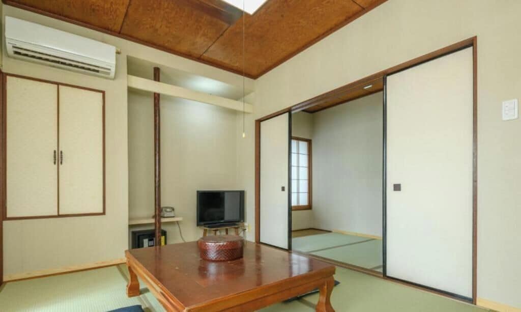 A traditional Japanese room with tatami flooring, a wooden table, a television, and sliding doors.