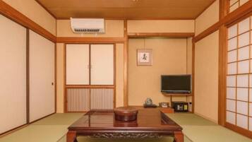 A traditional Japanese room with tatami flooring, a low wooden table, sliding doors, and a television.