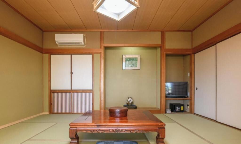 A traditional Japanese room with tatami flooring, a wooden table, sliding doors, and a television.