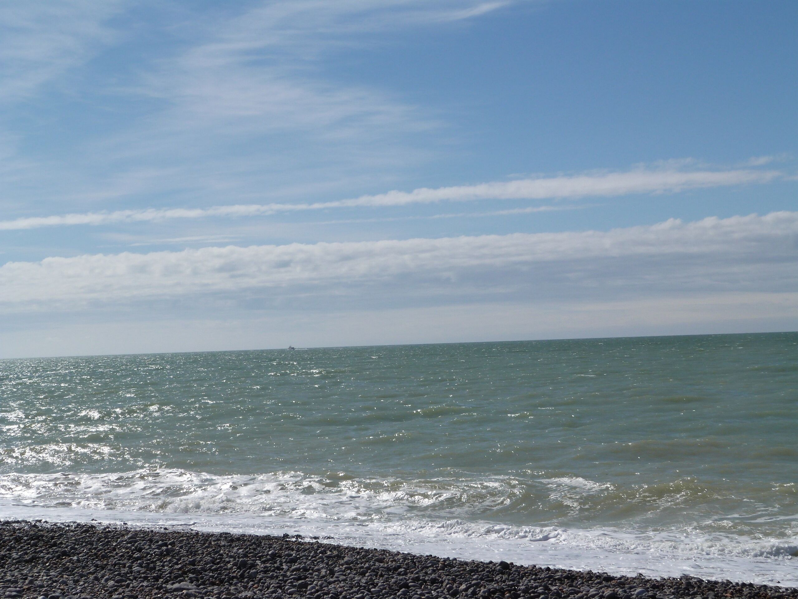 Ein Strand mit Kiesküste und ruhigem Meer unter blauem Himmel.