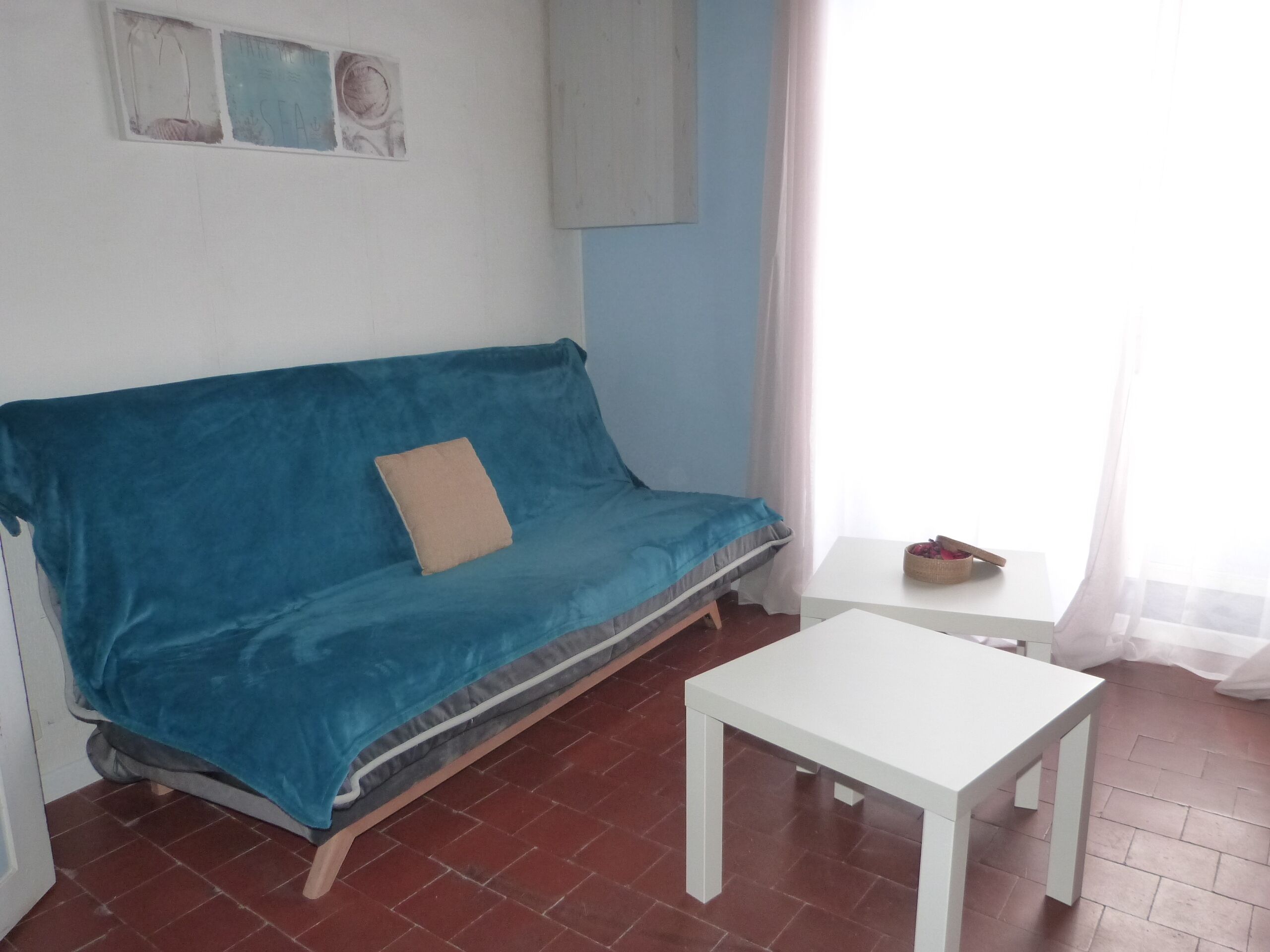 A room with a blue sofa, a white table, and a small window with curtains.