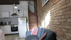 A cozy living area with a sofa, a kitchen in the background, and a brick wall. - Atypical fisherman's house for 6 person and a baby (Dieppe)