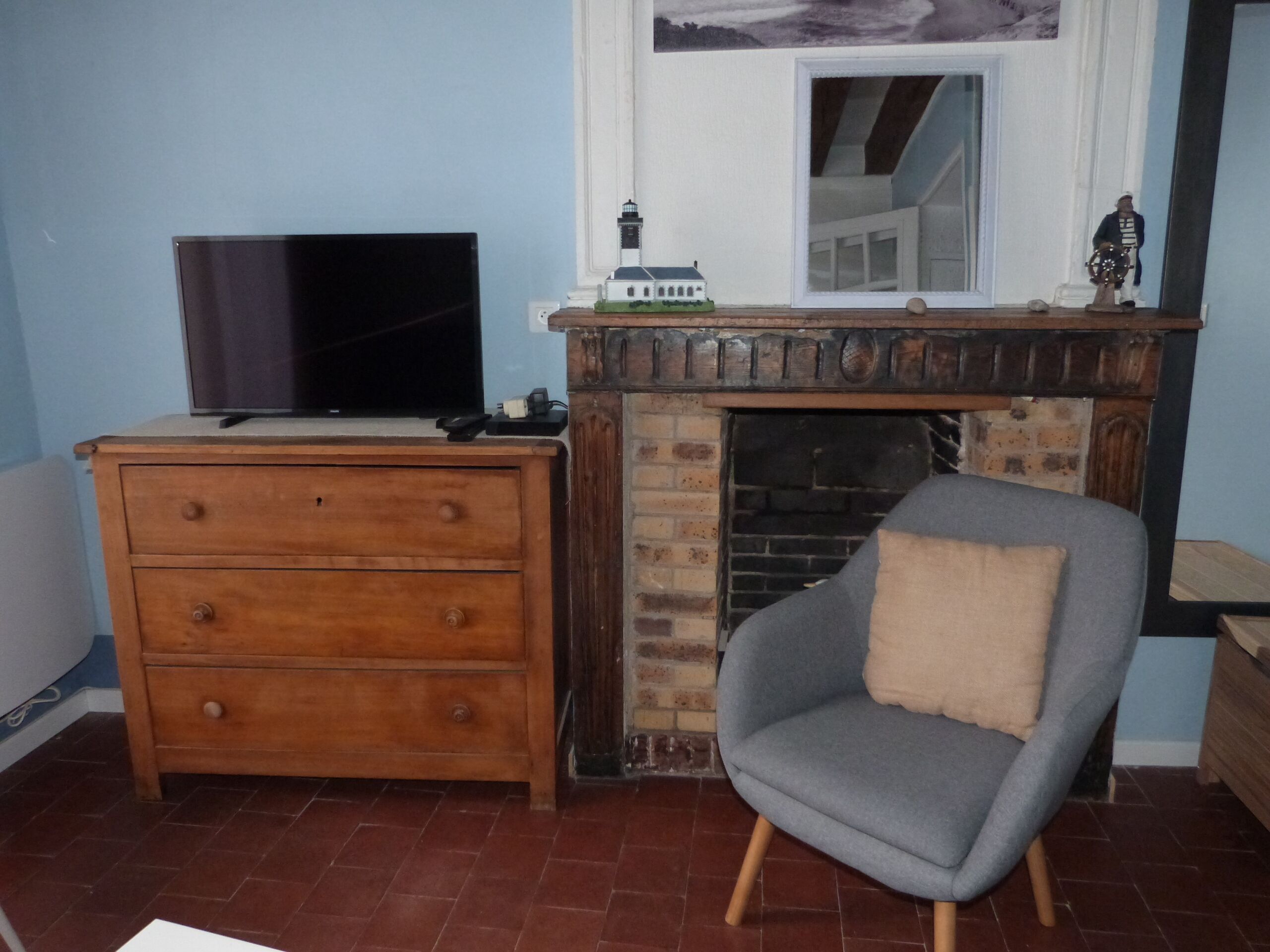 Habitació amb televisió damunt d'una petita taula de fusta, una poltrona gris amb coixí i una llar de pedra.