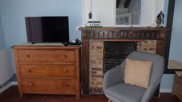 Habitació amb televisió damunt d'una petita taula de fusta, una poltrona gris amb coixí i una llar de pedra.