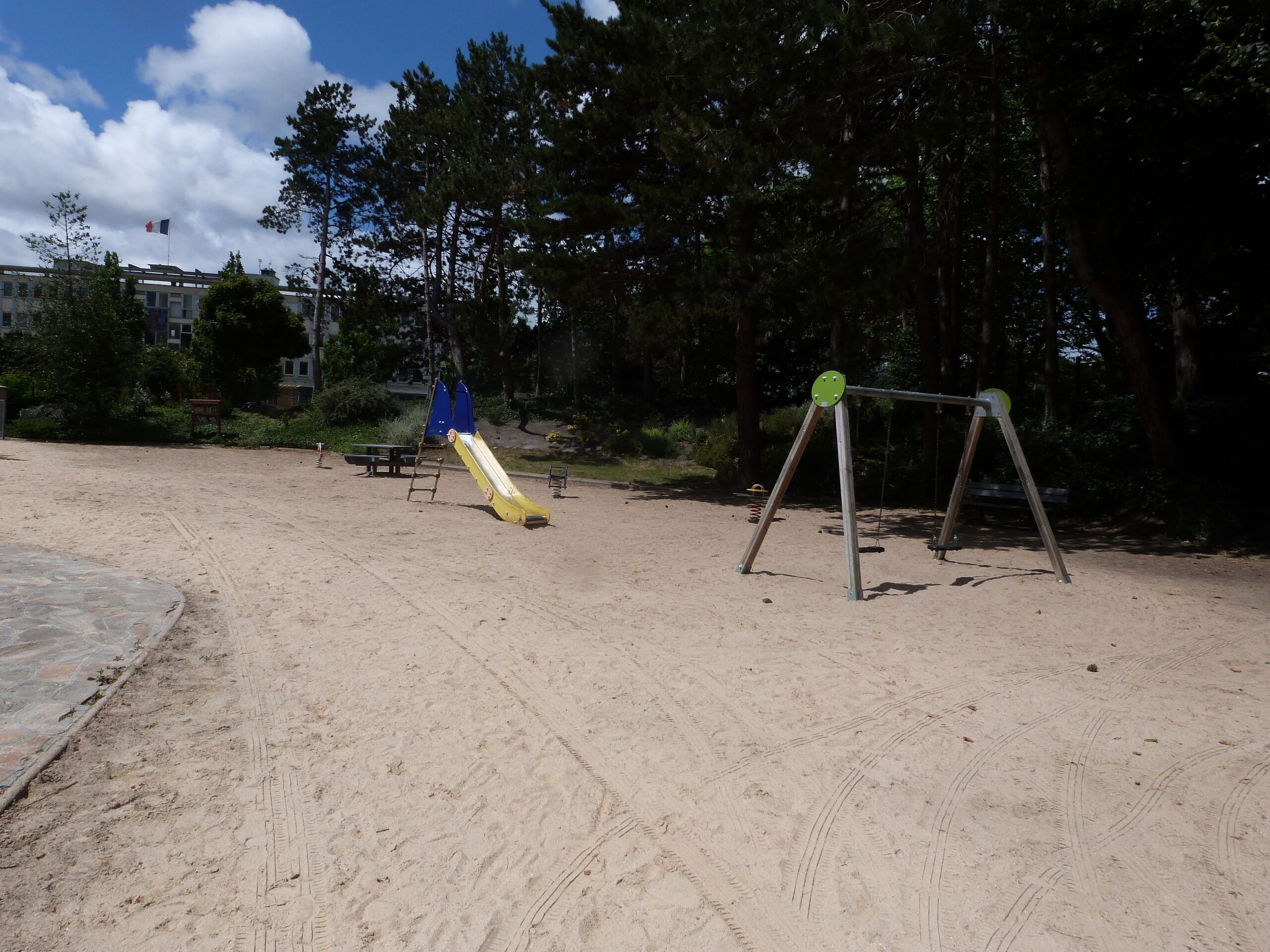 Ein Sandspielplatz mit Rutsche und Schaukeln.