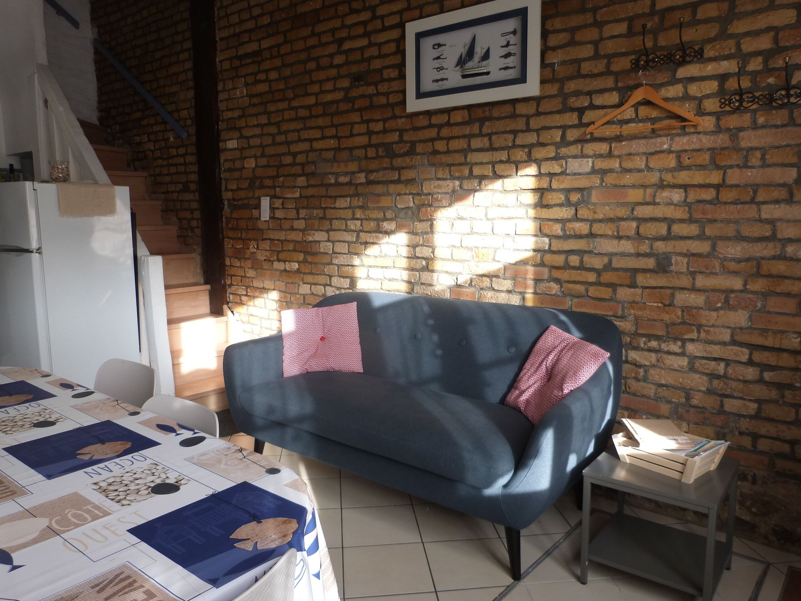 Una habitación con un sofá azul, una mesita pequeña, un mantel acolchado, una pared de ladrillo y un cuadro enmarcado.