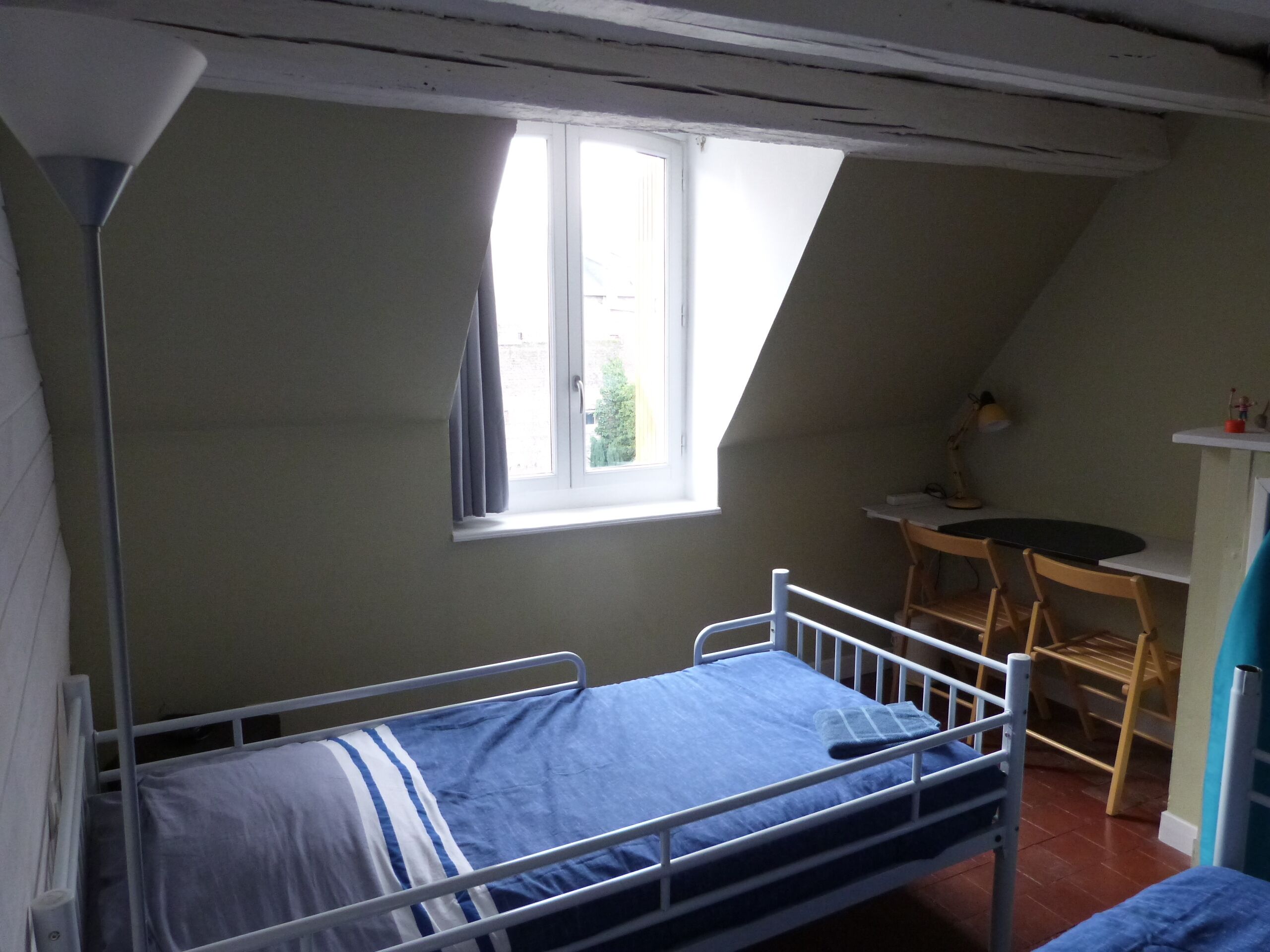 Une petite chambre avec un lit simple, un plafond en pente, une fenêtre, un bureau et une chaise.