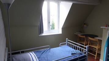 Une petite chambre avec un lit simple, un plafond en pente, une fenêtre, un bureau et une chaise.