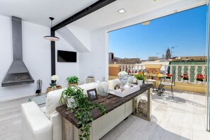 A modern kitchen with a large window, white furniture, and a view of the cityscape.
